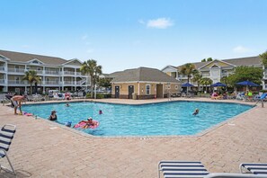 A swimming pool surrounded by lounge chairs and umbrellas, with a building in the background. - Havens 1136 Back on Program! Beautiful & Spacious! In Barefoot Resort! (North Myrtle Beach)