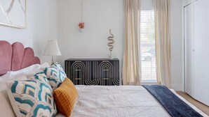 Un dormitorio con cama, cómoda, lámpara y ventana con cortinas.