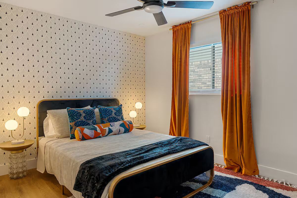 A bedroom with a bed, two bedside lamps, a ceiling fan, and a window with curtains.