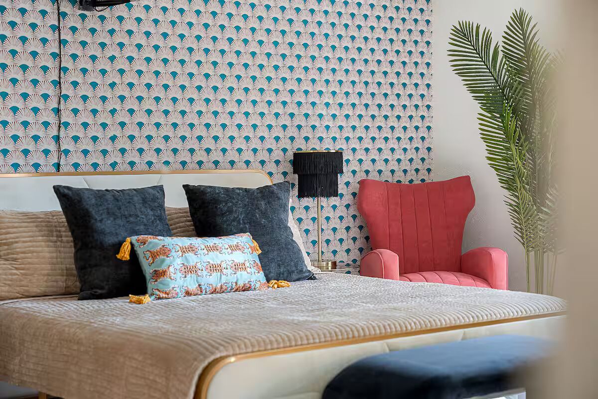 Una cama con un cabecero estampado, un sillón rojo y una planta alta.