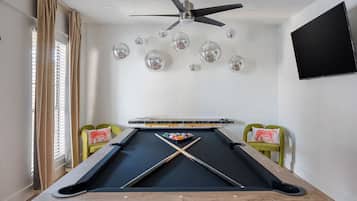Une table de billard, un ventilateur de plafond, des boules à facettes et un téléviseur fixé au mur.