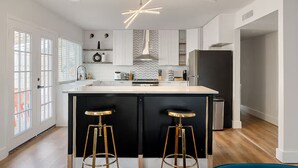 Una cocina moderna con una isla central, taburetes de bar y una lámpara de techo original.