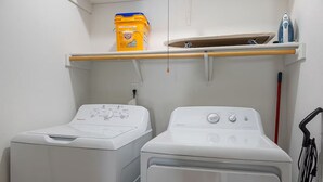 Un área de lavandería con dos lavadoras, un estante con un envase de detergente y un tendedero con un planchado.