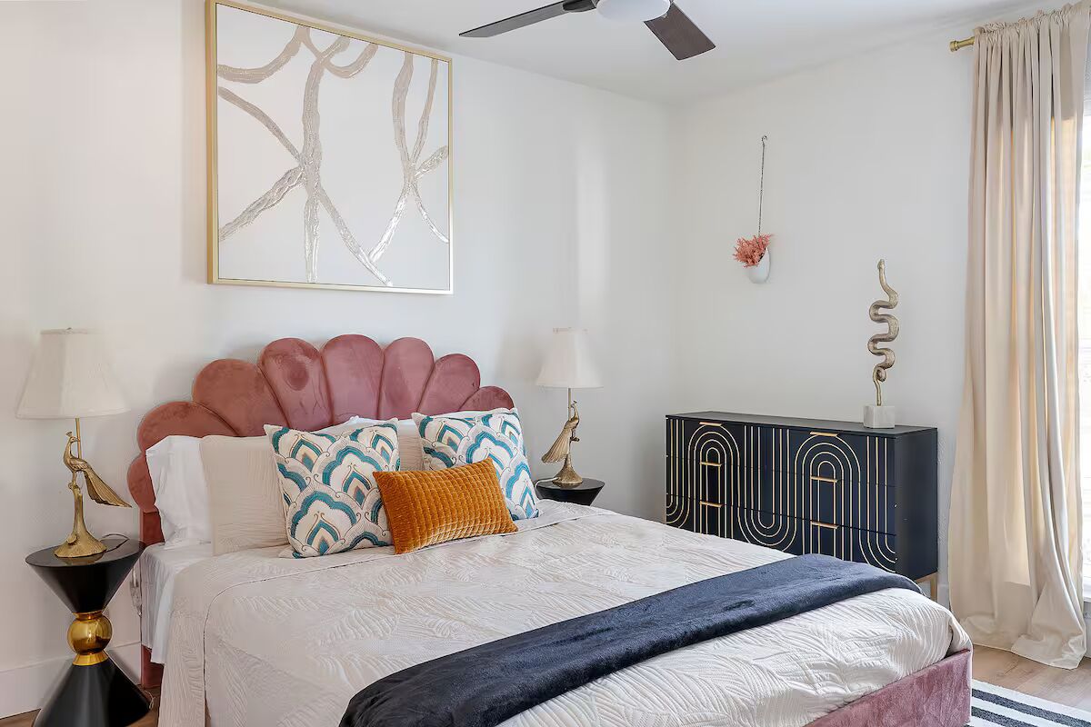 Una camera da letto con un letto, due comodini, una ventola a soffitto, un elemento decorativo a parete, un armadio e una finestra con tende.