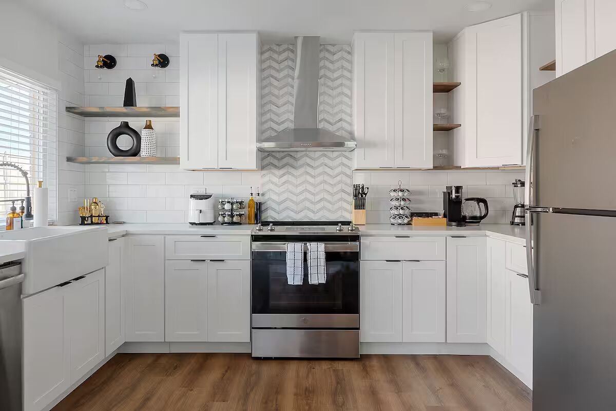 Una cucina moderna con mobili bianchi, forno in acciaio inossidabile e una schiena di cucina con motivo a spina di pesce.