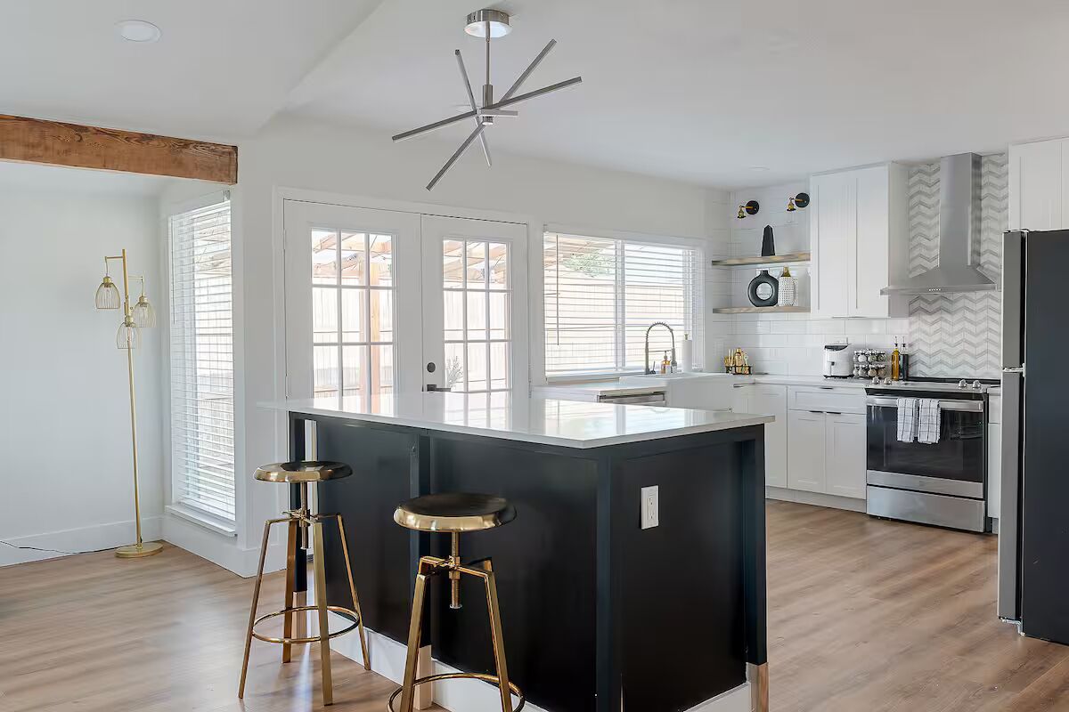 A modern kitchen with a central island, bar stools, a built-in oven, and a large window.