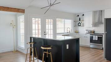 A modern kitchen with a central island, bar stools, a built-in oven, and a large window.