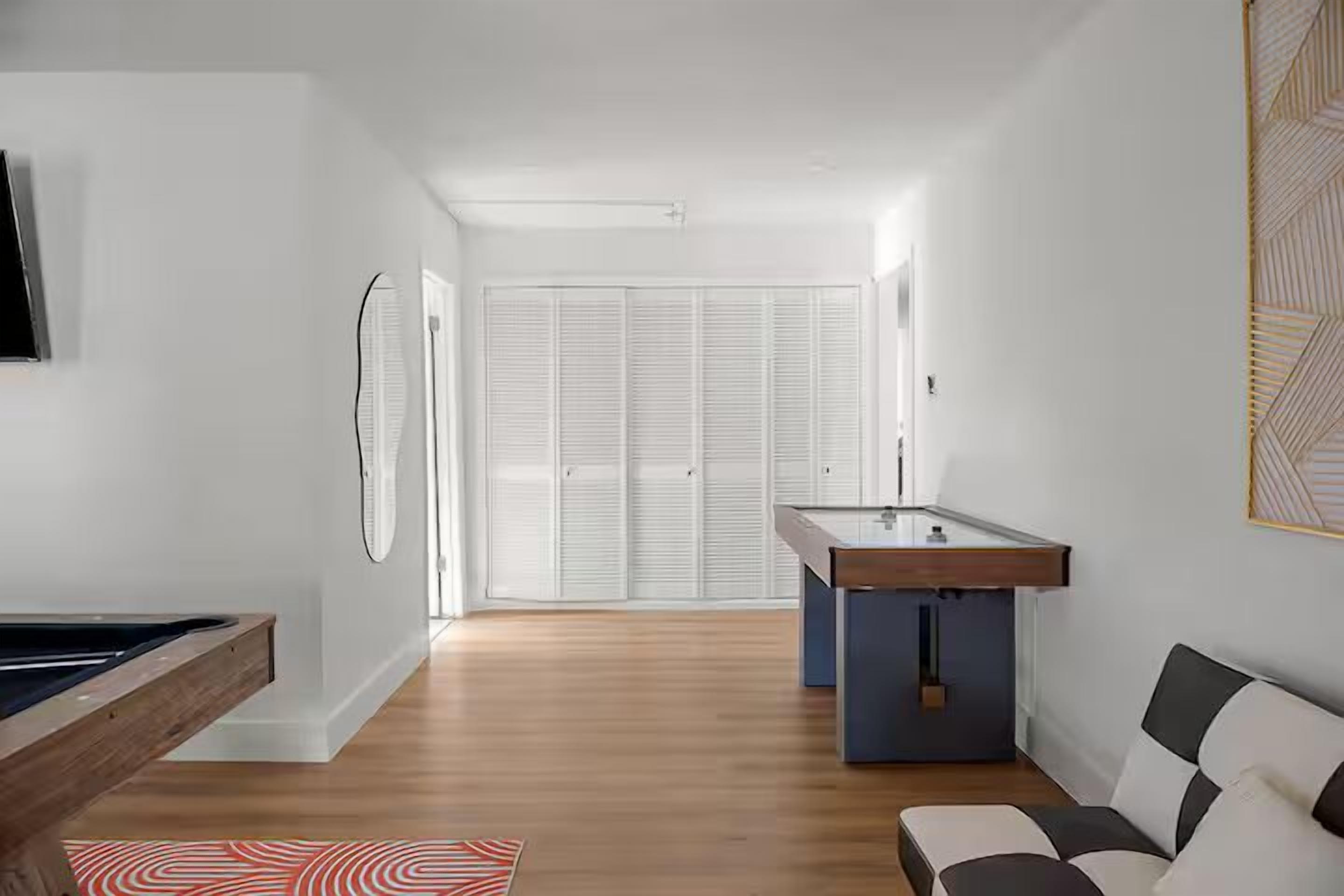 Una habitación moderna con mesa de billar, un sofá y vistas a un armario blanco.