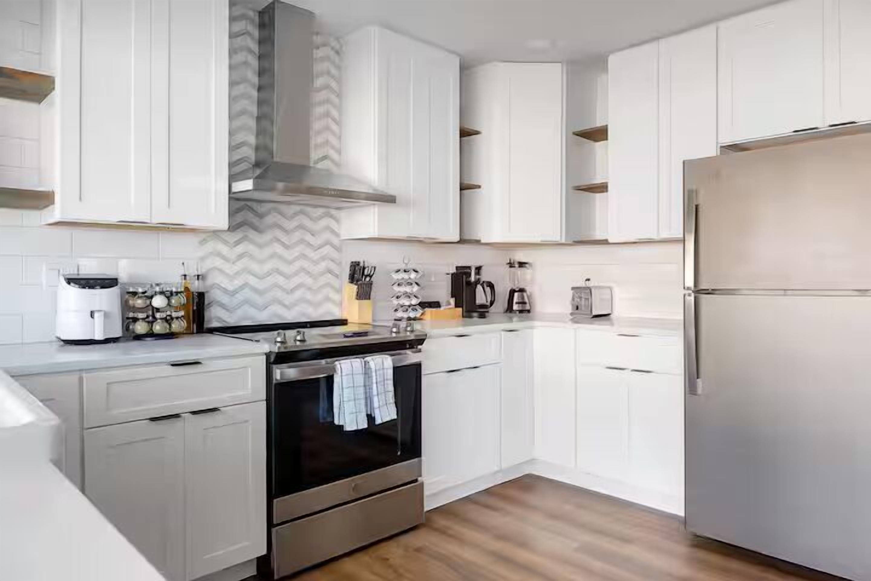 Una cocina moderna con armarios blancos, un refrigerador de acero inoxidable y un horno empotrado.