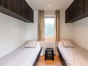 Ein Schlafzimmer mit zwei Einzelbetten, einem Fenster mit Vorhängen, einem Heizkörper und einem Hocker.