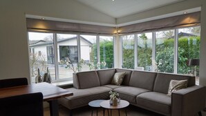 A modern living room with a sectional sofa, a round coffee table, and large windows offering a view of the outdoors. - --------deluxe 4 People---------- (Noordwijk)