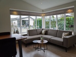 Ein modernes Wohnzimmer mit Ecksofa, rundem Couchtisch und großen Fenstern, die einen Blick ins Freie bieten.
