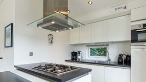 A modern kitchen with a central island, stainless steel appliances, and a window providing a view. - --------deluxe 4 People---------- (Noordwijk)