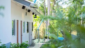 A building with a white exterior, multiple doors, and a pathway leading to a fenced area with greenery. - Fix25House Koh Kood (Ko Kood)