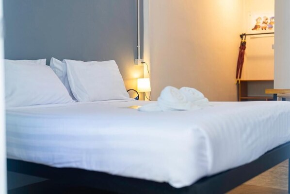 Una cama bien hecha con sábanas blancas, una lámpara de noche y una toalla sobre la cama.