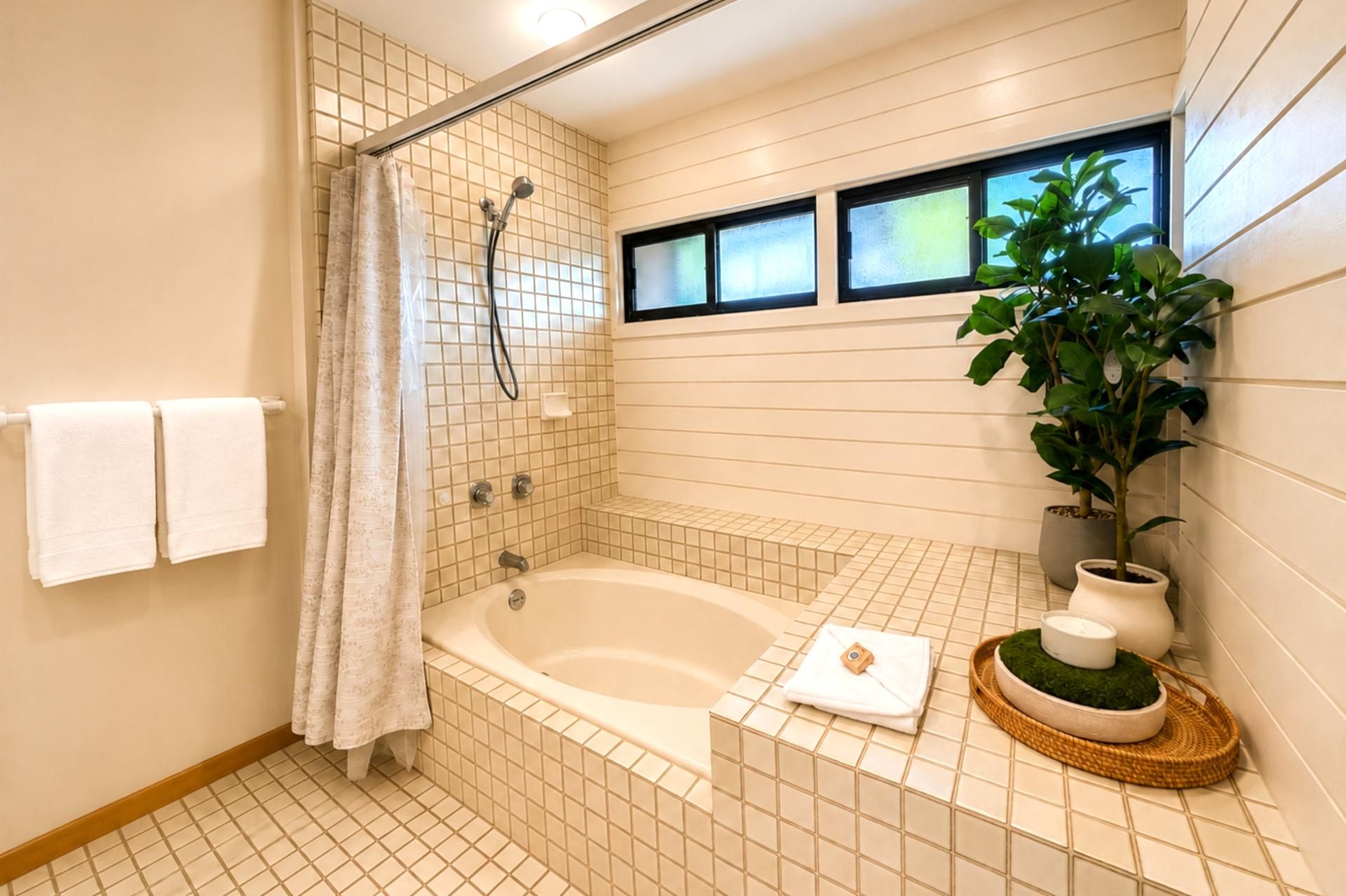 A bathroom with a bathtub, shower, and potted plants.