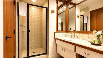 A bathroom with a glass-enclosed shower, a sink with a mirror, and a vase with flowers on the counter.