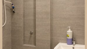 A bathroom with a shower, a sink, and a hand soap dispenser.