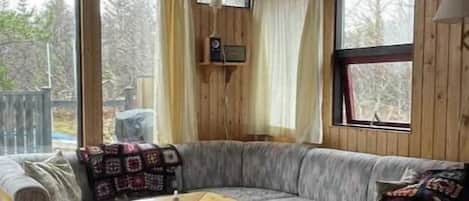 A wooden interior with a sofa, a table, and large windows.