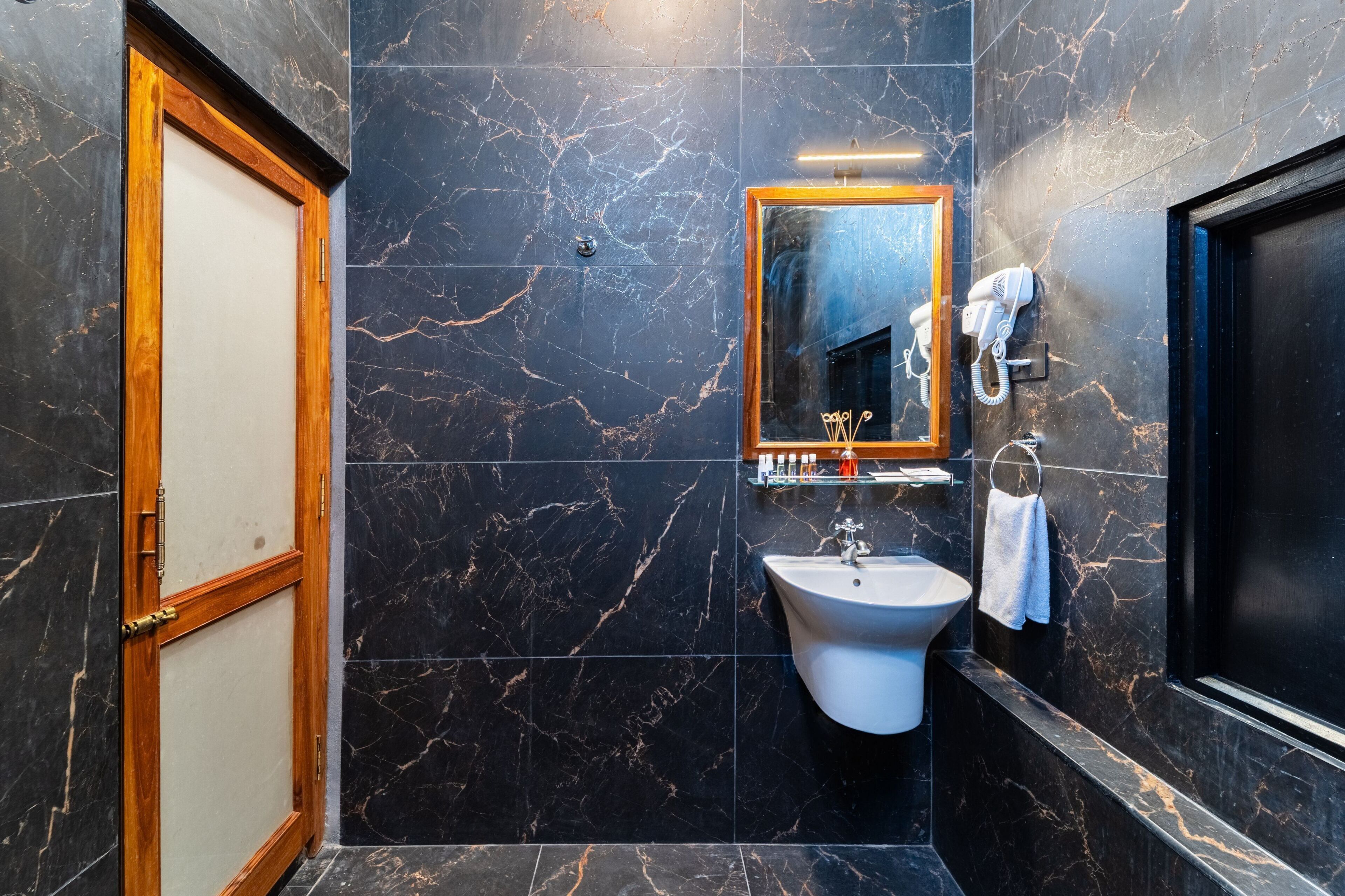 A bathroom with a marble wall, a sink, a mirror, and a towel rack.