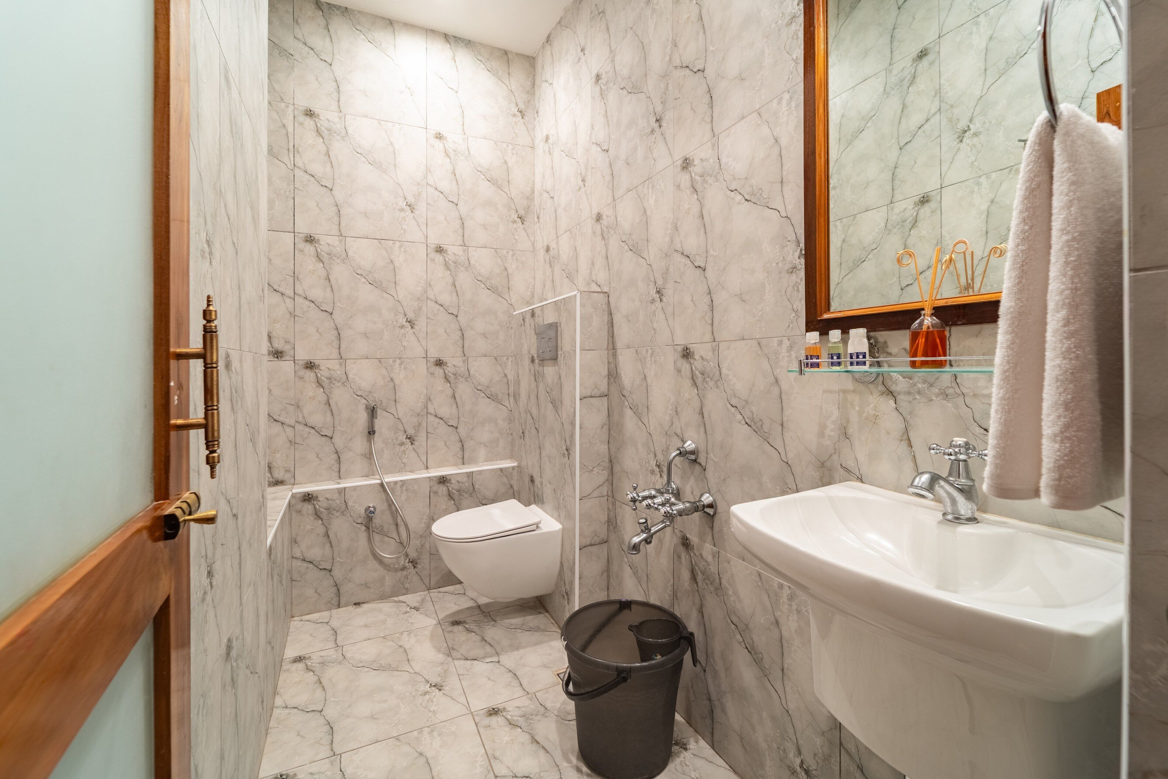 A bathroom with a marble wall, a white sink, a toilet, and a shower area.