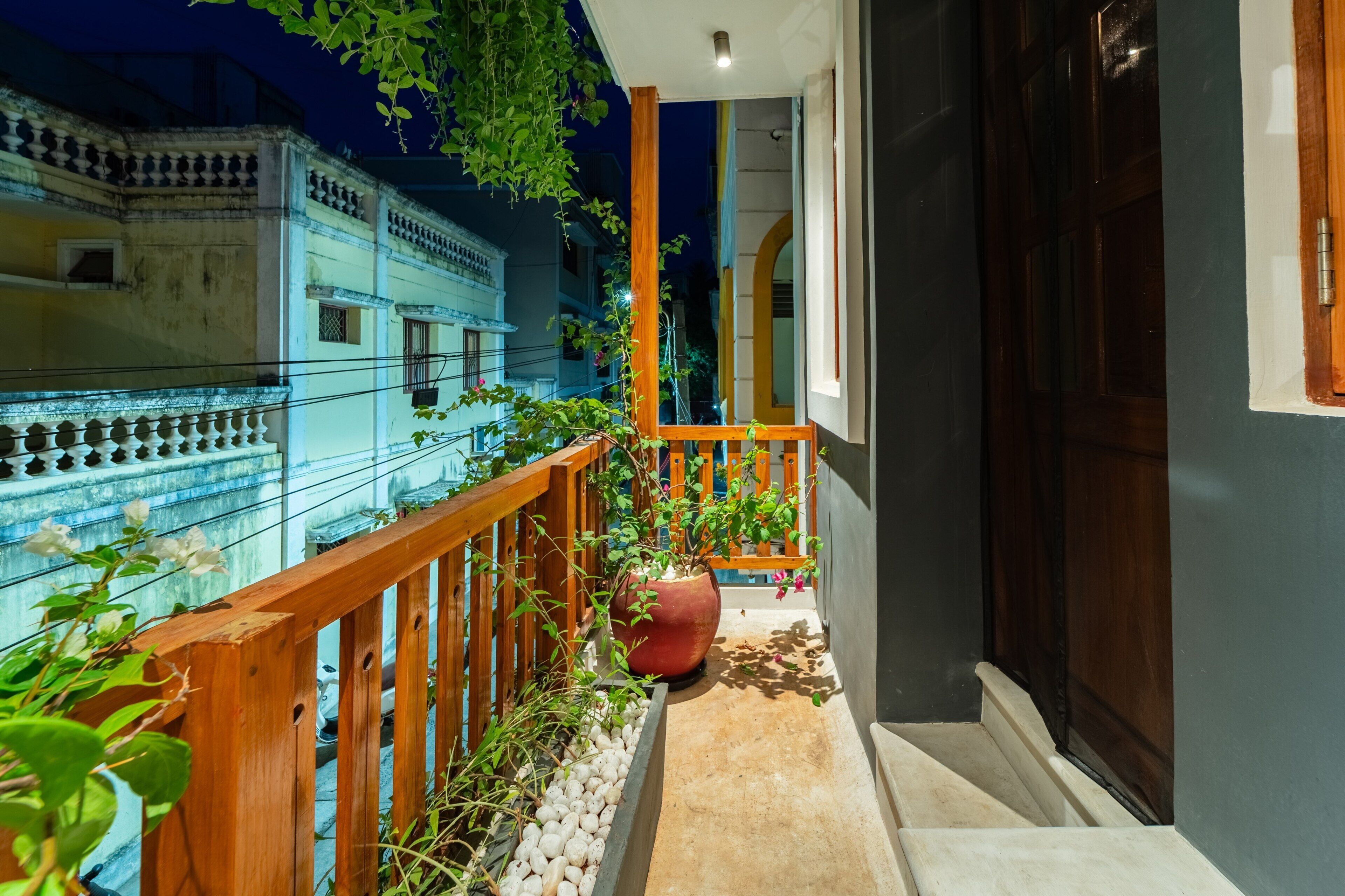 Un balcon étroit doté d’une balustrade en bois, de plantes en pot et offrant une vue sur les bâtiments voisins.