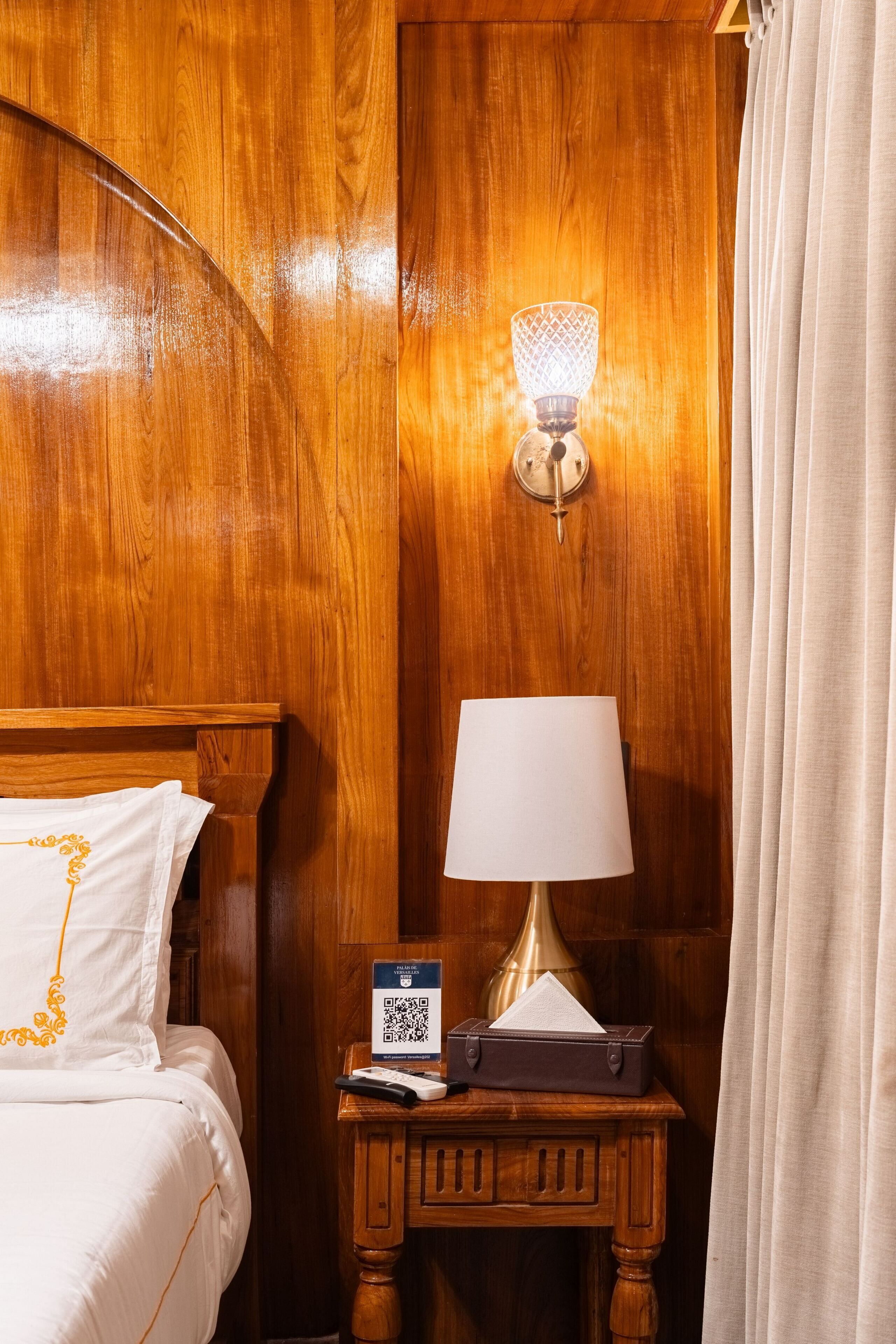 A wooden room with a bed, a nightstand with a lamp, and a QR code sign.