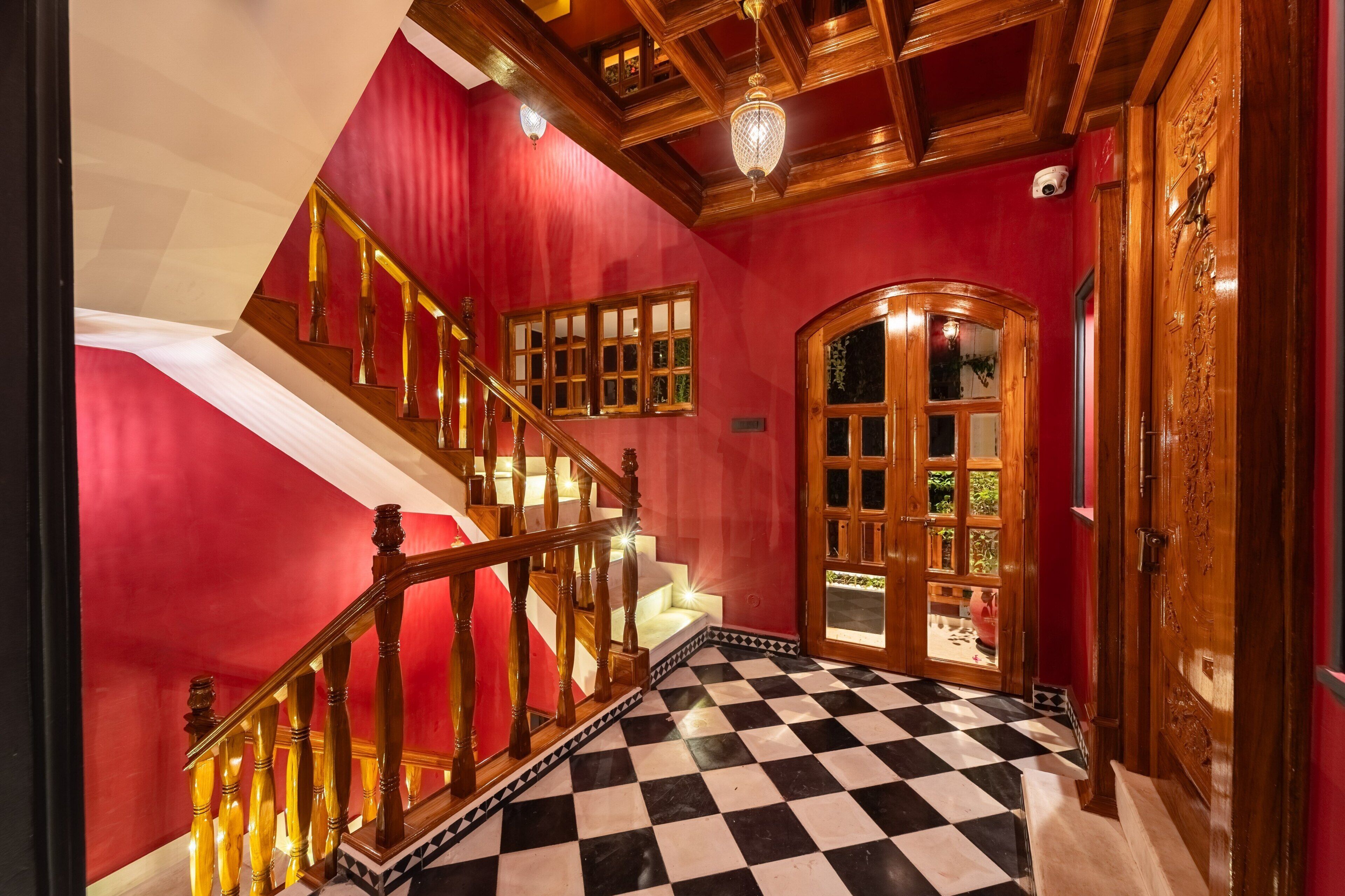 Un escalier dont les marches sont recouvertes d’un motif à carreaux, menant à une pièce aux murs rouges et dotée d’une porte en bois avec des panneaux de verre.
