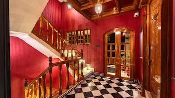Un escalier dont les marches sont recouvertes d’un motif à carreaux, menant à une pièce aux murs rouges et dotée d’une porte en bois avec des panneaux de verre.