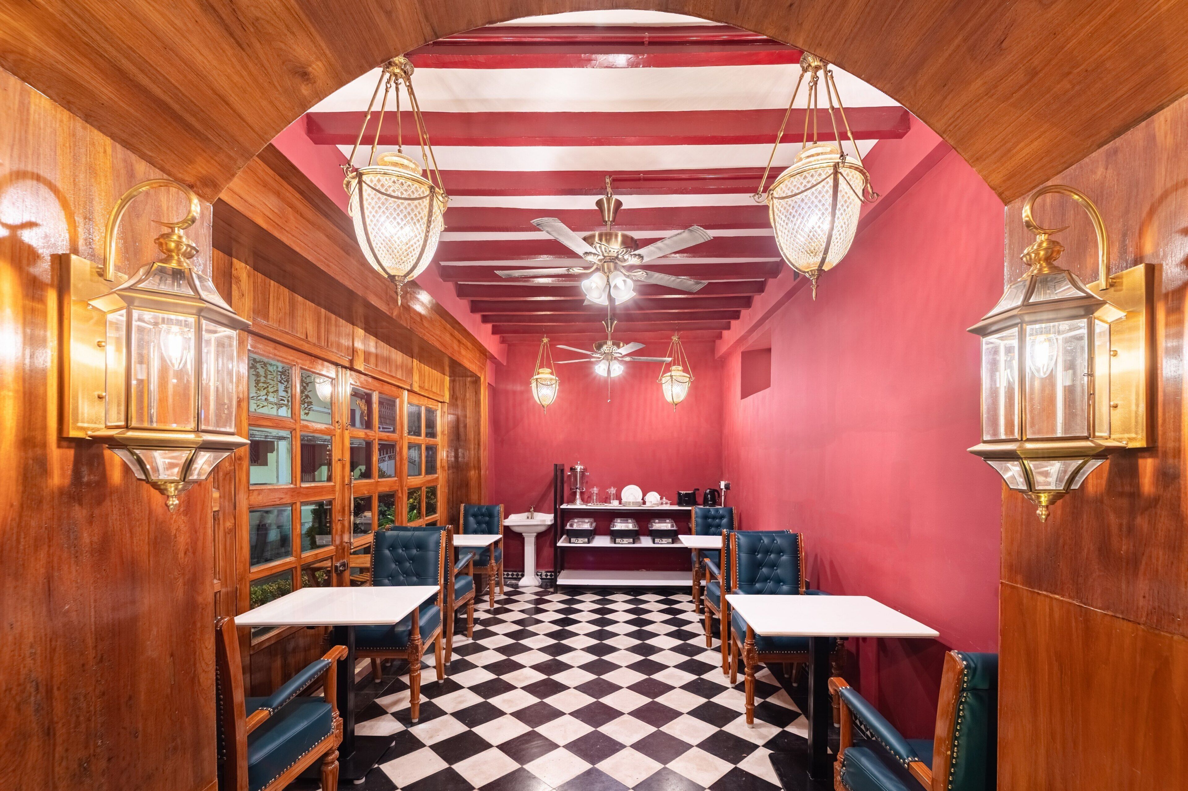 A room with a checkered floor, wooden walls, and a red ceiling. There are tables and chairs arranged for dining.