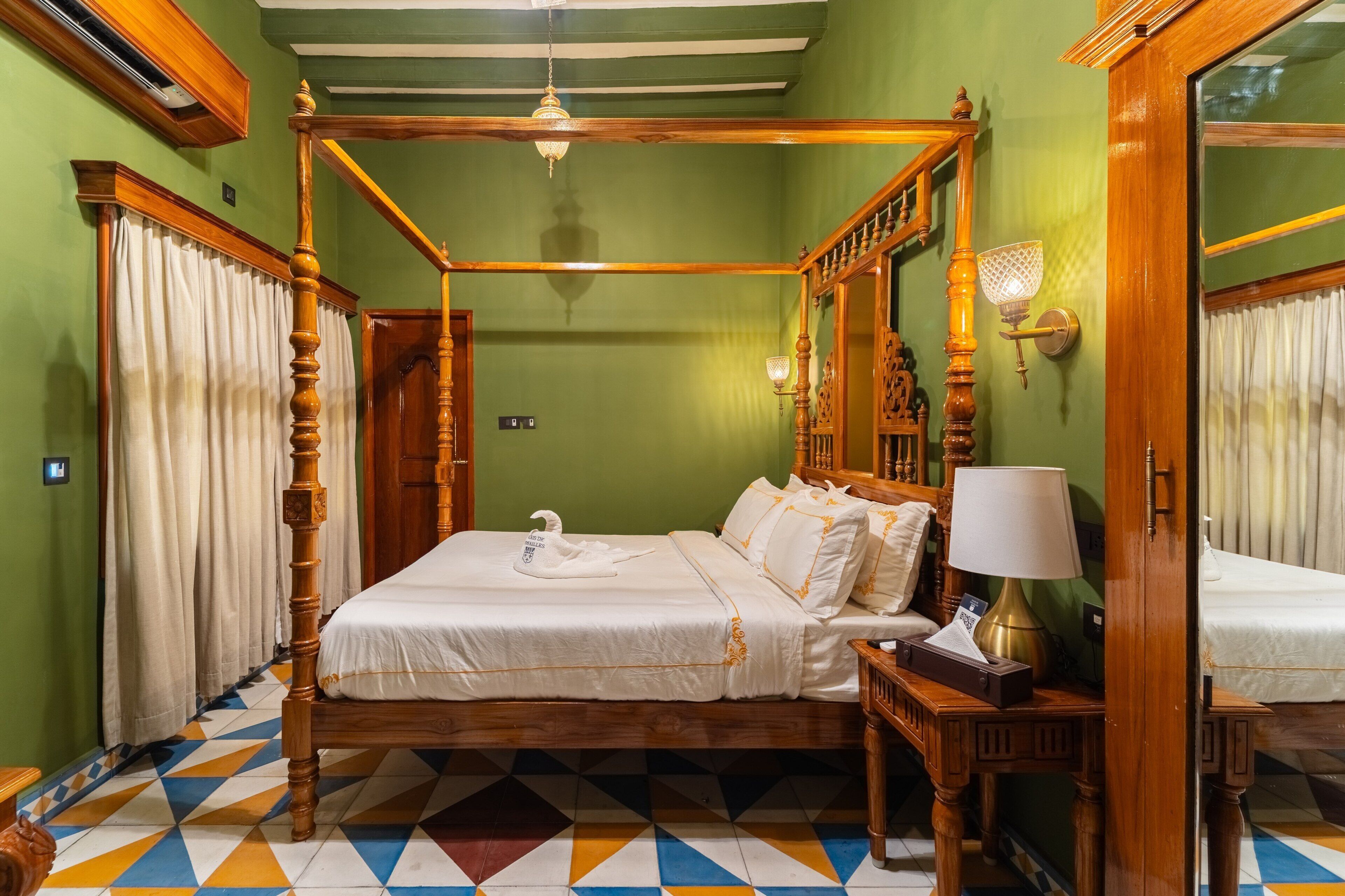 A four-poster bed with a swan-shaped pillow, a bedside table with a lamp, and a mirror on the wall.
