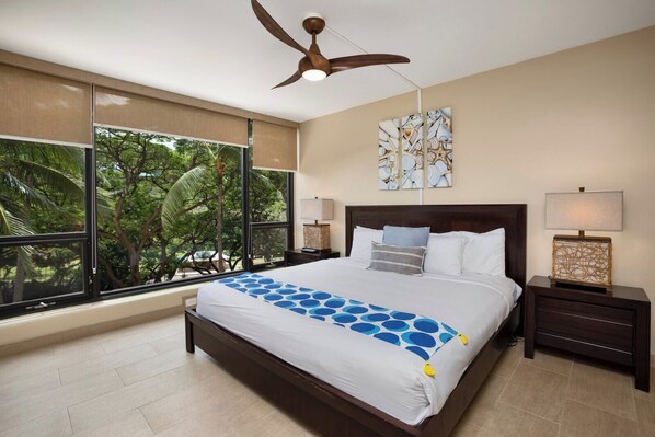 A bedroom with a large bed, a ceiling fan, a window with a view of trees, and artwork on the wall. - Mahana | 2 Oceanfront Villas, Sleeps 8 | Car Incl. w/ 6+ Nights | ML-4199 by KBM (Lahaina)
