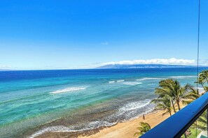 Blick auf einen Strand mit klarem Wasser, sandigem Ufer und Palmen.
