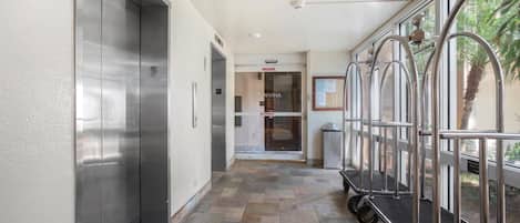 A hallway with a glass door entrance, a trash bin, and a cart.