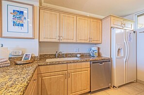 A kitchen with wooden cabinets, a granite countertop, a stainless steel dishwasher, and a refrigerator. - Mahana | 3 Oceanfront Villas, Sleeps 10 | Car Incl. w/ 6+ Nights | ML-4208 by KBM (Lahaina)