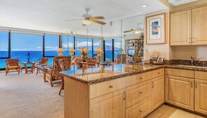 A spacious kitchen with a large island, wooden cabinets, and a view of the ocean. - Mahana | 3 Oceanfront Villas, Sleeps 10 | Car Incl. w/ 6+ Nights | ML-4208 by KBM (Lahaina)