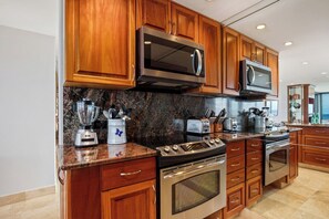 A modern kitchen with wooden cabinets, stainless steel appliances, granite countertops, and a built-in oven. - Mahana | 4 Oceanfront Villas, Sleeps 14 | Car Incl. w/ 6+ Nights | ML-4211 by KBM (Lahaina)