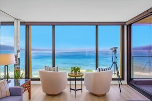A modern room with large windows, two sofas, a small table, and a tripod. - Mahana | 4 Oceanfront Villas, Sleeps 14 | Car Incl. w/ 6+ Nights | ML-4211 by KBM (Lahaina)