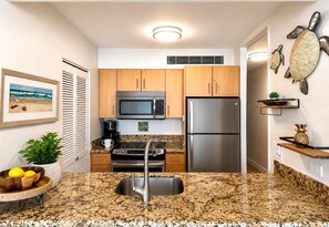 A compact kitchen with wooden cabinets, a stainless steel refrigerator, a microwave, and a coffee maker. - Mahana | 3 Oceanfront Villas, Sleeps 10 | Car Incl. w/ 6+ Nights | ML-4214 by KBM (Lahaina)