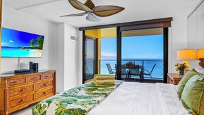 A hotel room with a bed, a TV, a wooden dresser, a balcony with a table and chairs, and a view of the ocean. - Mahana | 3 Oceanfront Villas, Sleeps 10 | Car Incl. w/ 6+ Nights | ML-4214 by KBM (Lahaina)