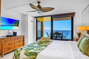 Ein Hotelzimmer mit einem Bett, einem Fernseher, einer Holzkommode, einem Balkon mit Tisch und Stühlen sowie Meerblick.