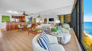 A modern living room with a dining area, kitchen, and large windows overlooking the ocean. - Mahana | 3 Oceanfront Villas, Sleeps 10 | Car Incl. w/ 6+ Nights | ML-4214 by KBM (Lahaina)