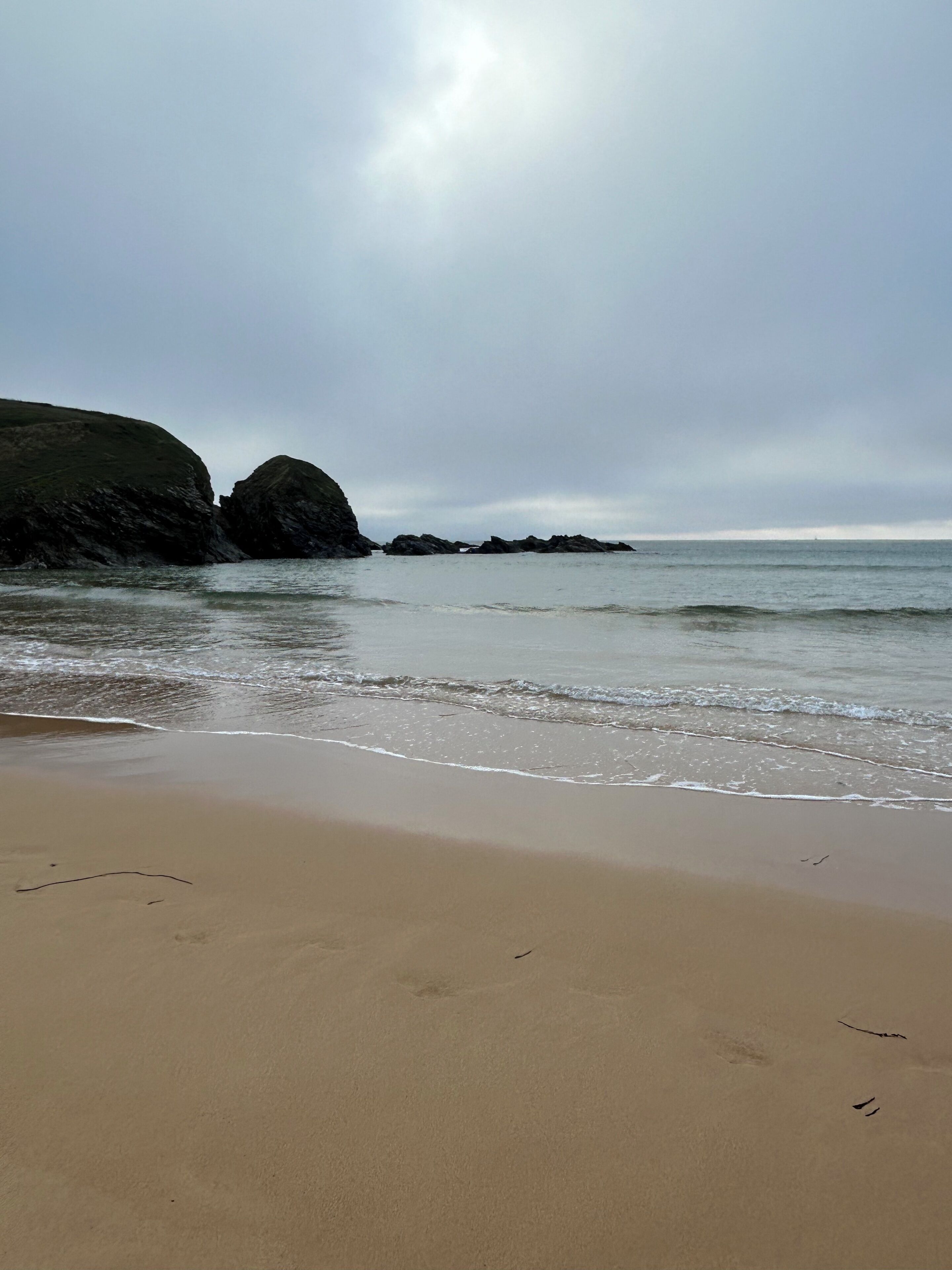 A beach with a sandy shore and rocky outcrops in the background.