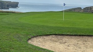 Campo de golf con un mástil de bandera, un búnker de arena y vista al mar.