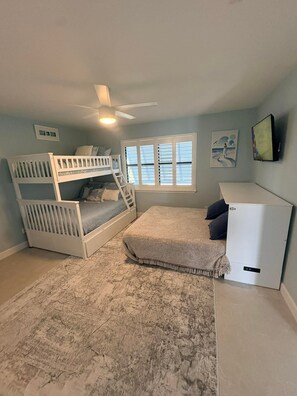 Ein Zimmer mit Etagenbetten, Deckenventilator, Fenster mit Jalousien und einem kleinen weißen Schrank.