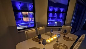 Mesa de jantar com design moderno, com louças postas, copos de vinho e luminária central.