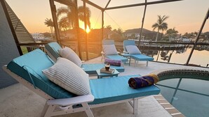 Uma área de estar ao ar livre banhada pelo sol, com piscina, espreguiçadeiras e vista para o pôr do sol.