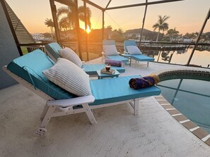 Eine sonnige Außenlounge mit Pool, Liegestühlen und Blick auf den Sonnenuntergang.