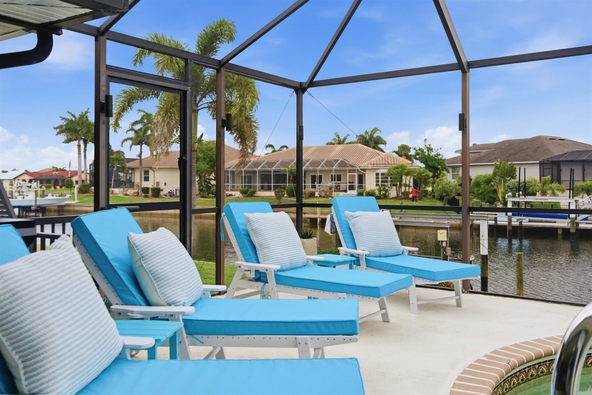 A covered outdoor area with lounge chairs and a view of a body of water and houses in the background.