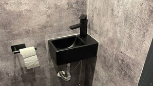 Une petite salle de bain avec un lavabo noir, des toilettes et un seau bleu.